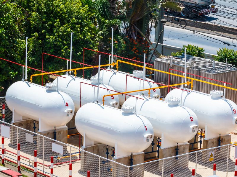 Eight, white, pill-shaped tanks surrounded by a chain link fence.