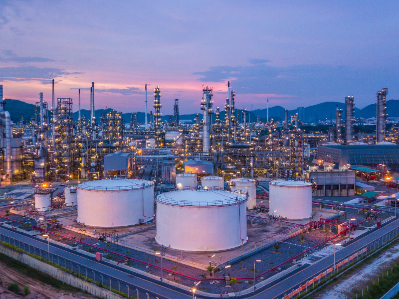 A large factory in the mountains with a purple and pink sky.