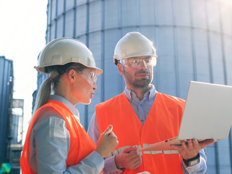 Two people wearing hardhats looking at a computer.