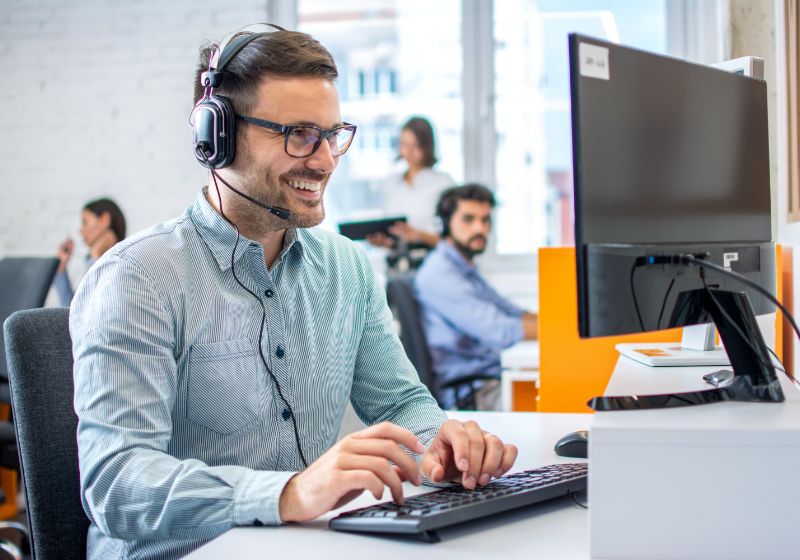 A person wearing a headset typing on a computer.